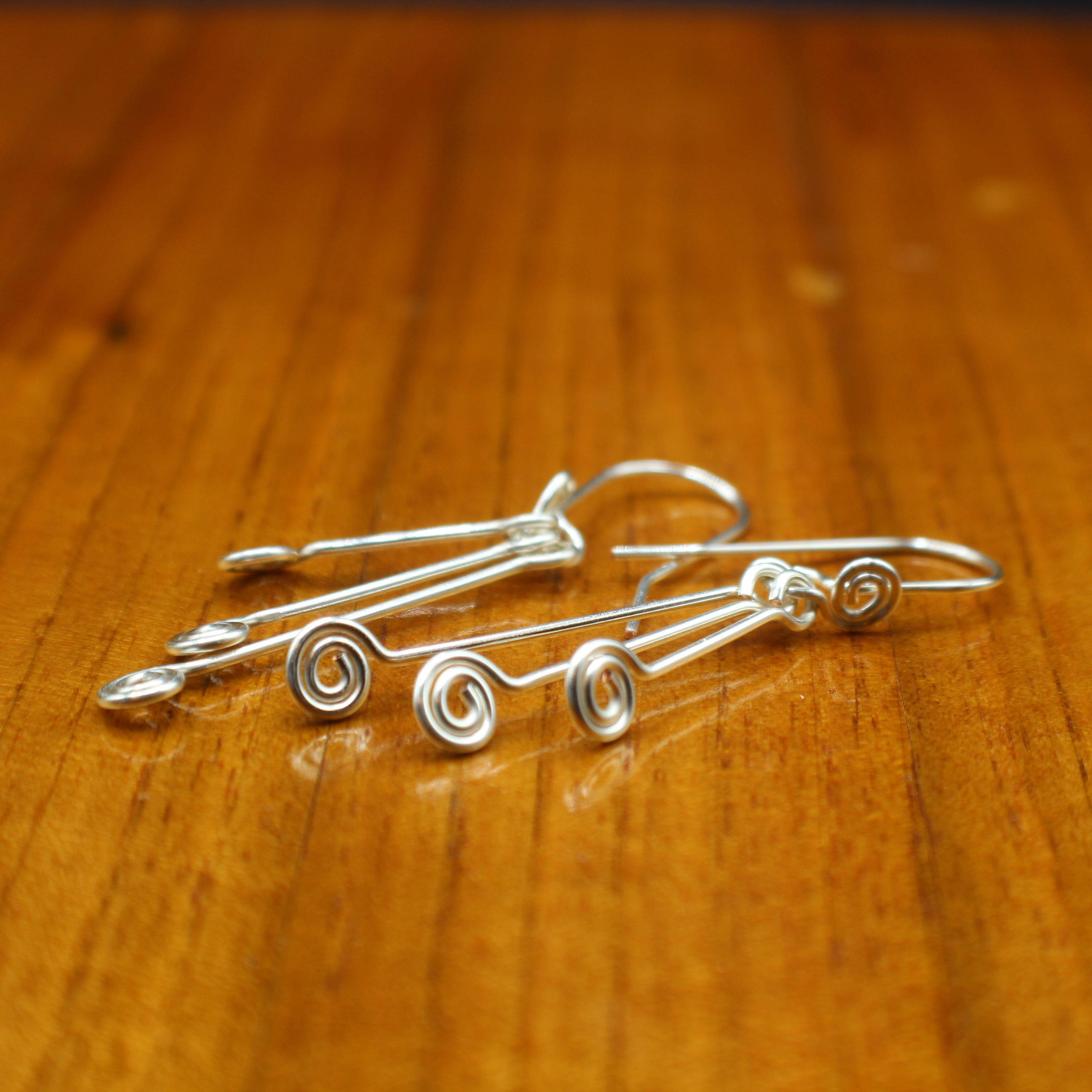 Silver wire earrings with spiral designs on a wooden surface