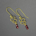 Freeform brass wire earrings with red faceted beads on a gray background