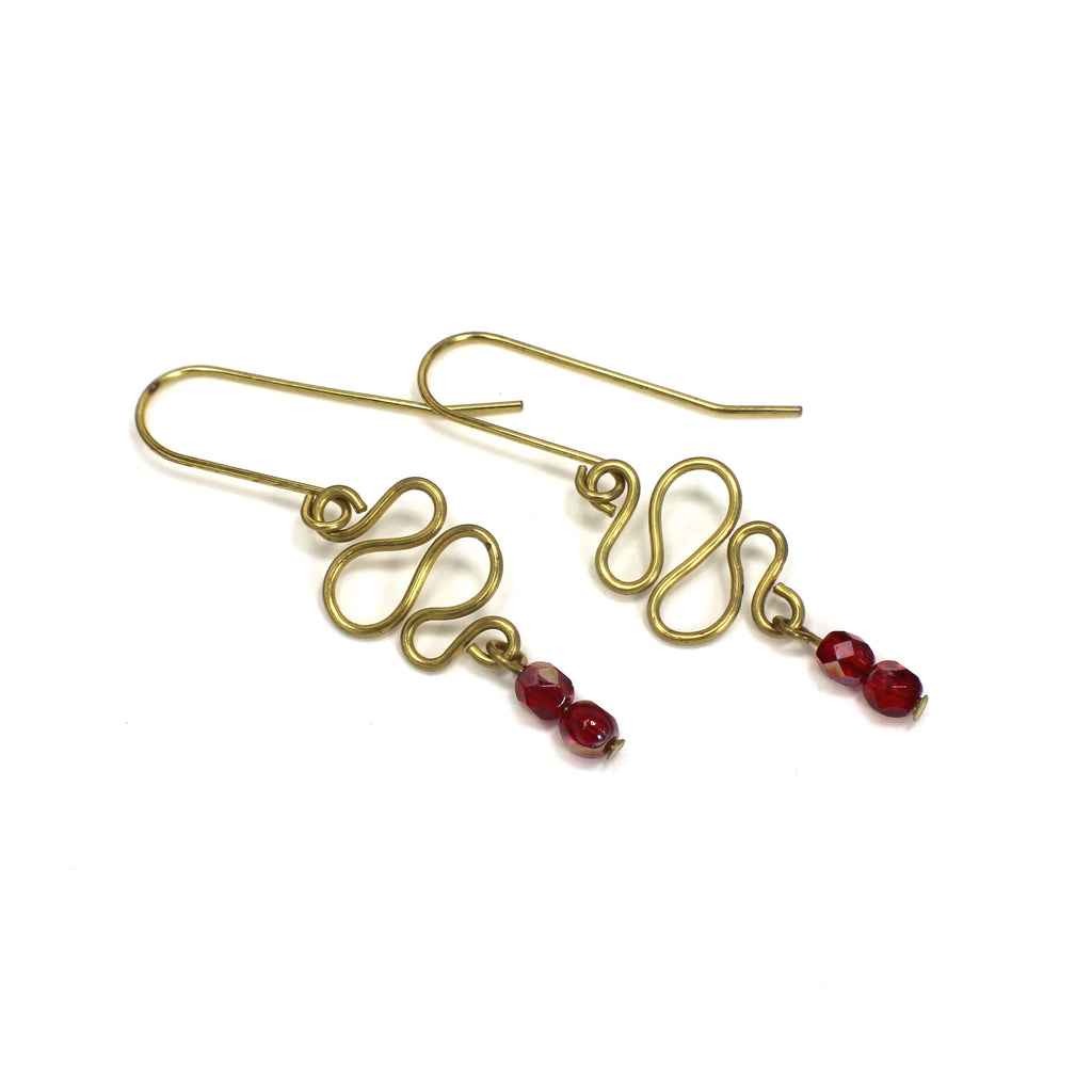 Freeform brass wire earrings with red faceted beads on a white background