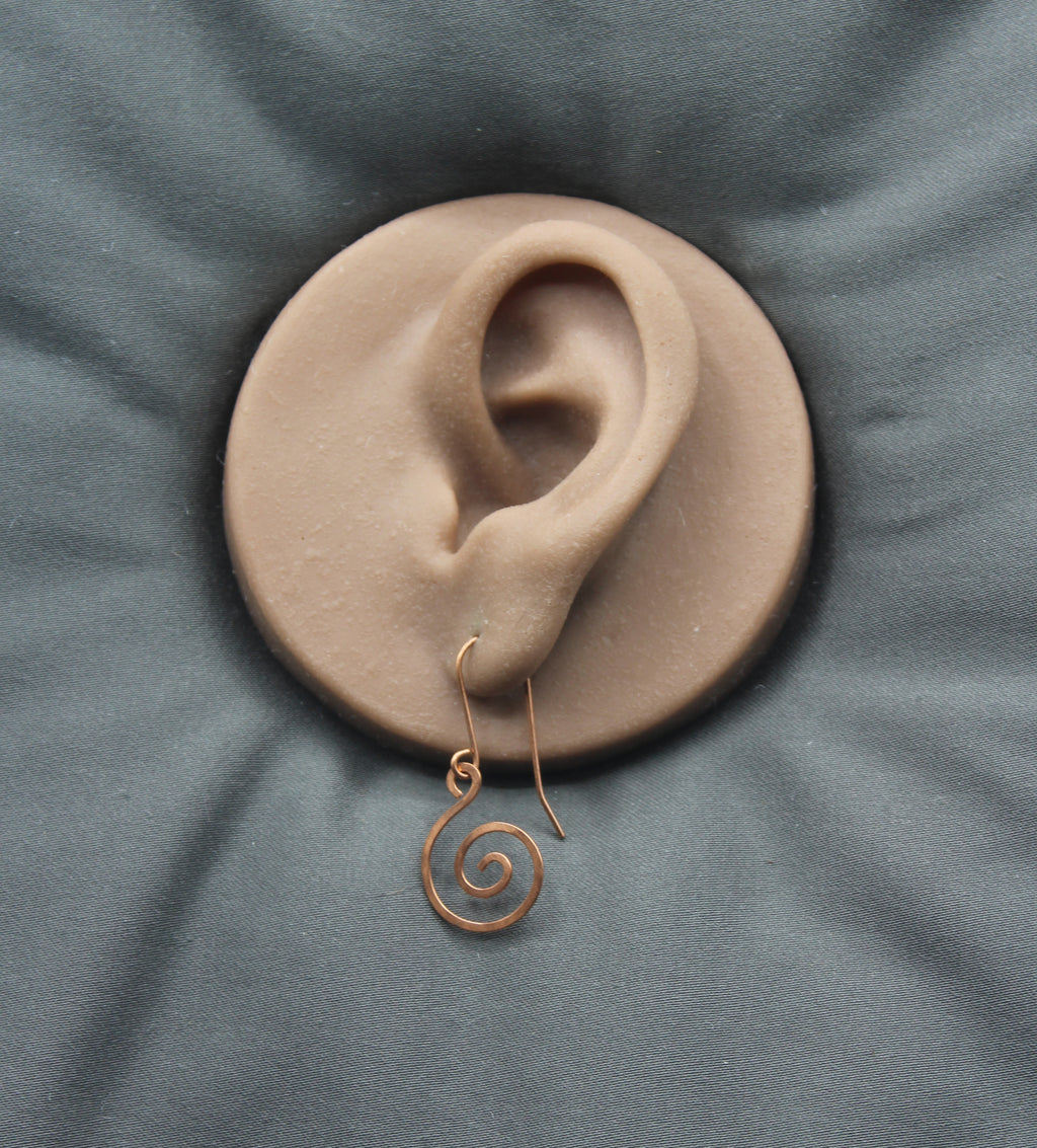 Clay model of an ear with a copper spiral earring on a gray fabric background