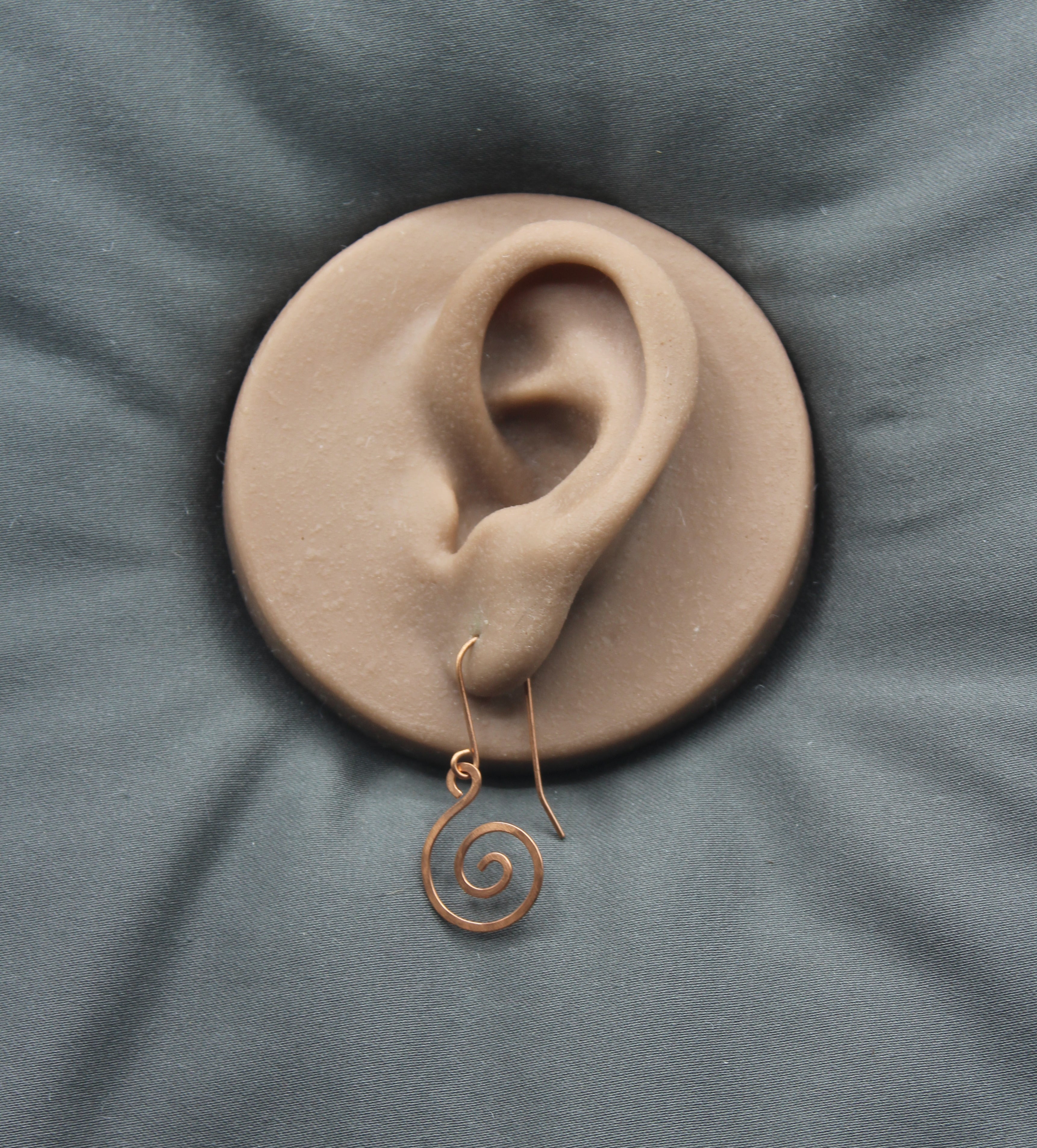 Clay model of an ear with a copper spiral earring on a gray fabric background