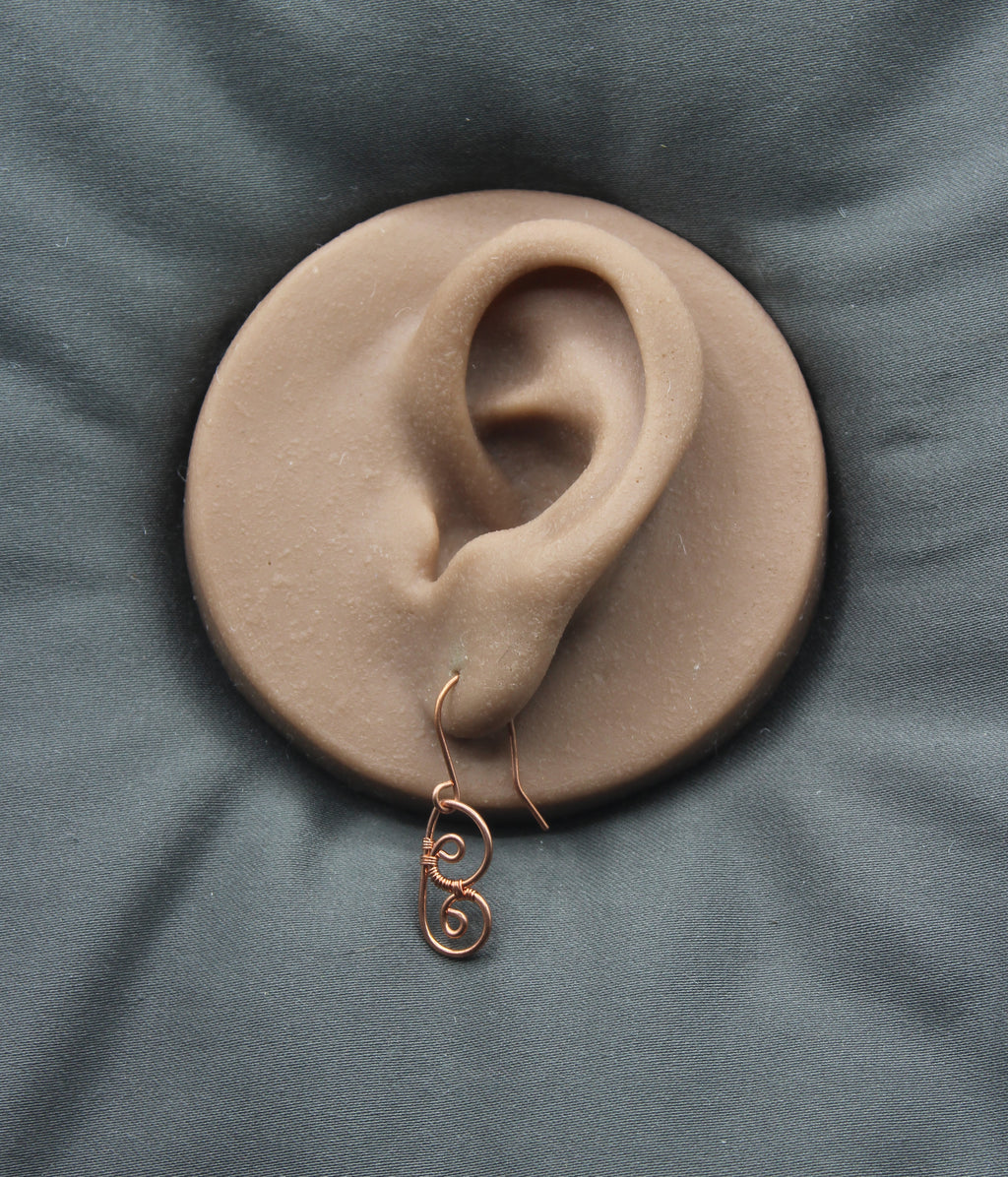 Copper wire earring shaped as an abstract butterfly wing, on a clay model of an ear against a gray background