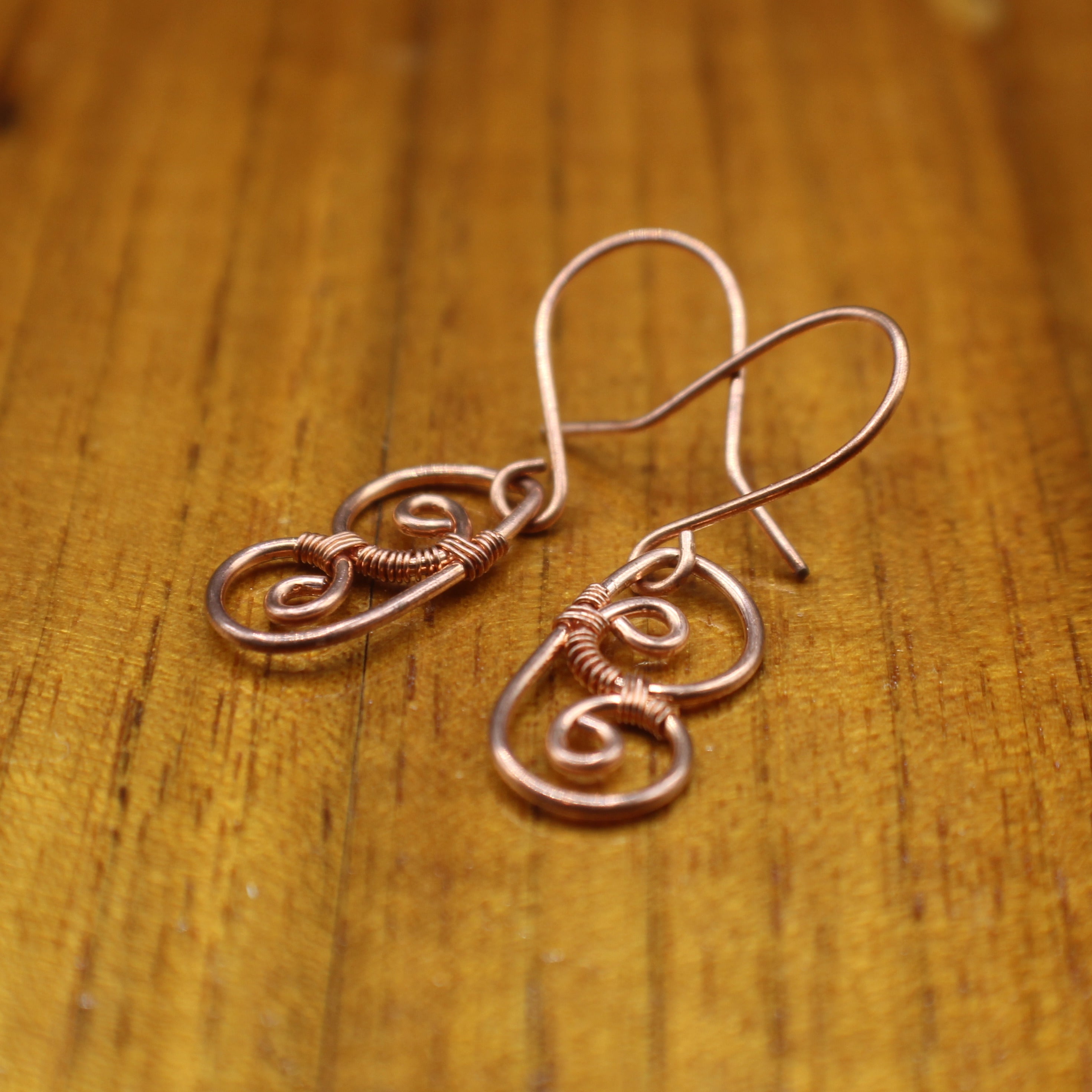 Copper wire earrings shaped as abstract butterfly wings lying on a wooden surface