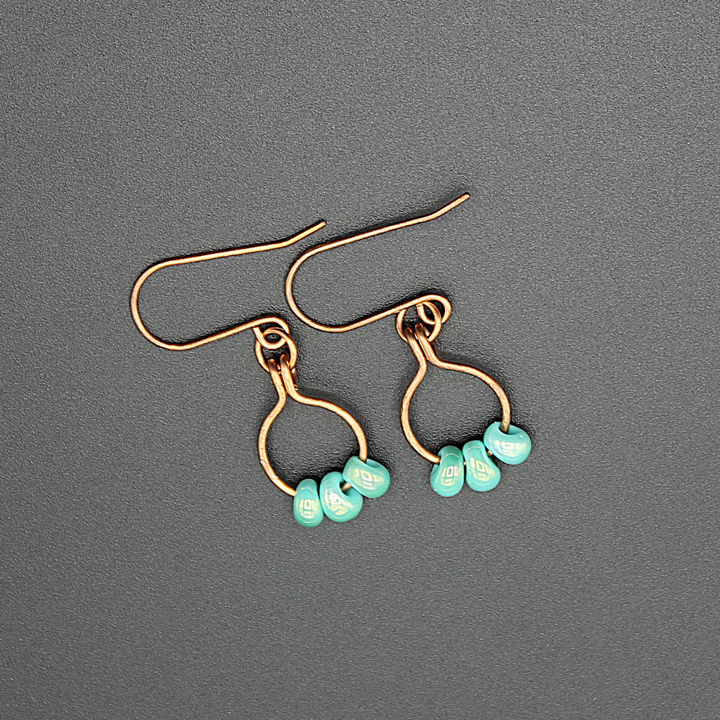 Copper wire earrings with turquoise beads hanging from small hoops on a gray background