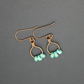 Copper wire earrings with turquoise beads hanging from small hoops on a gray background
