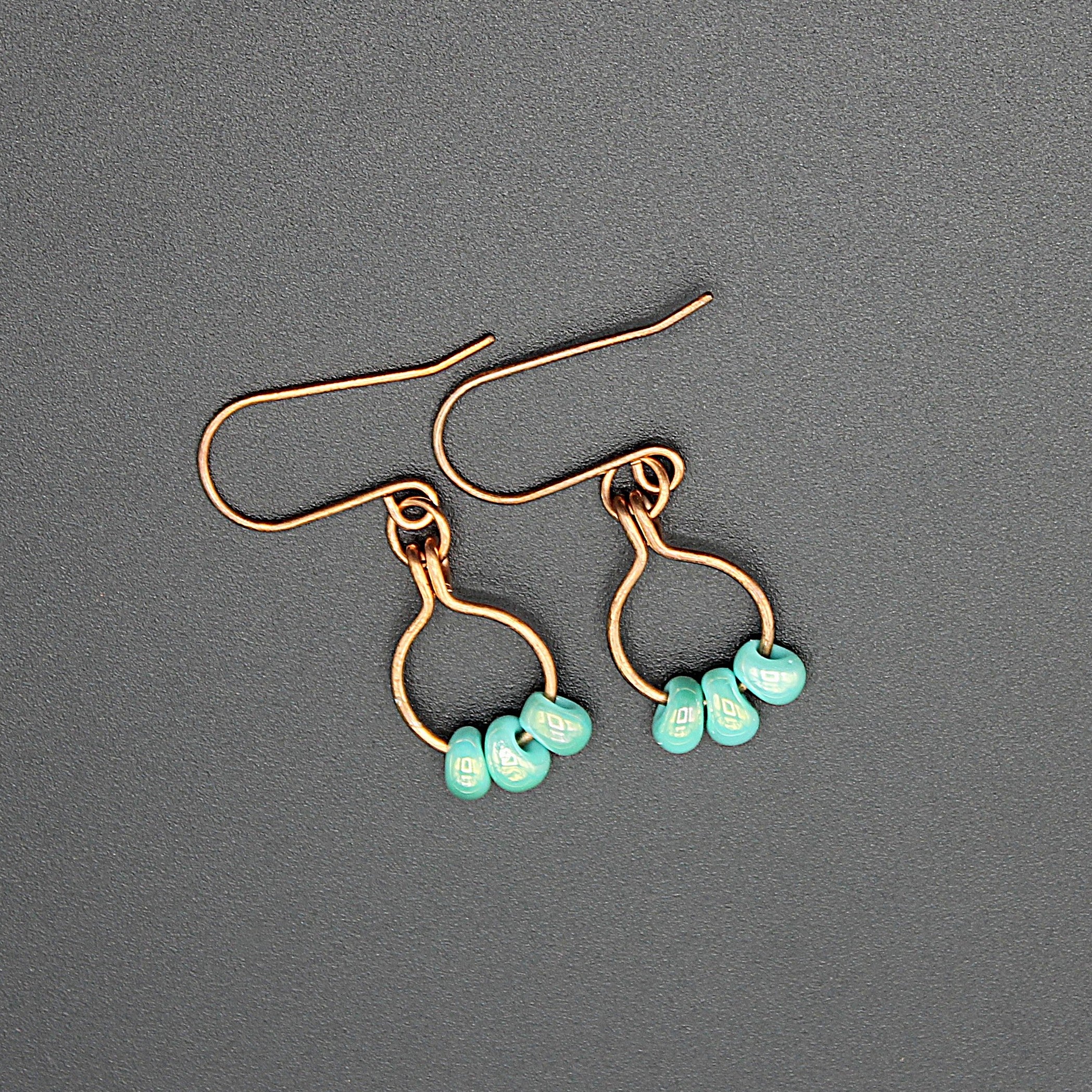 Copper wire earrings with turquoise beads hanging from small hoops on a gray background