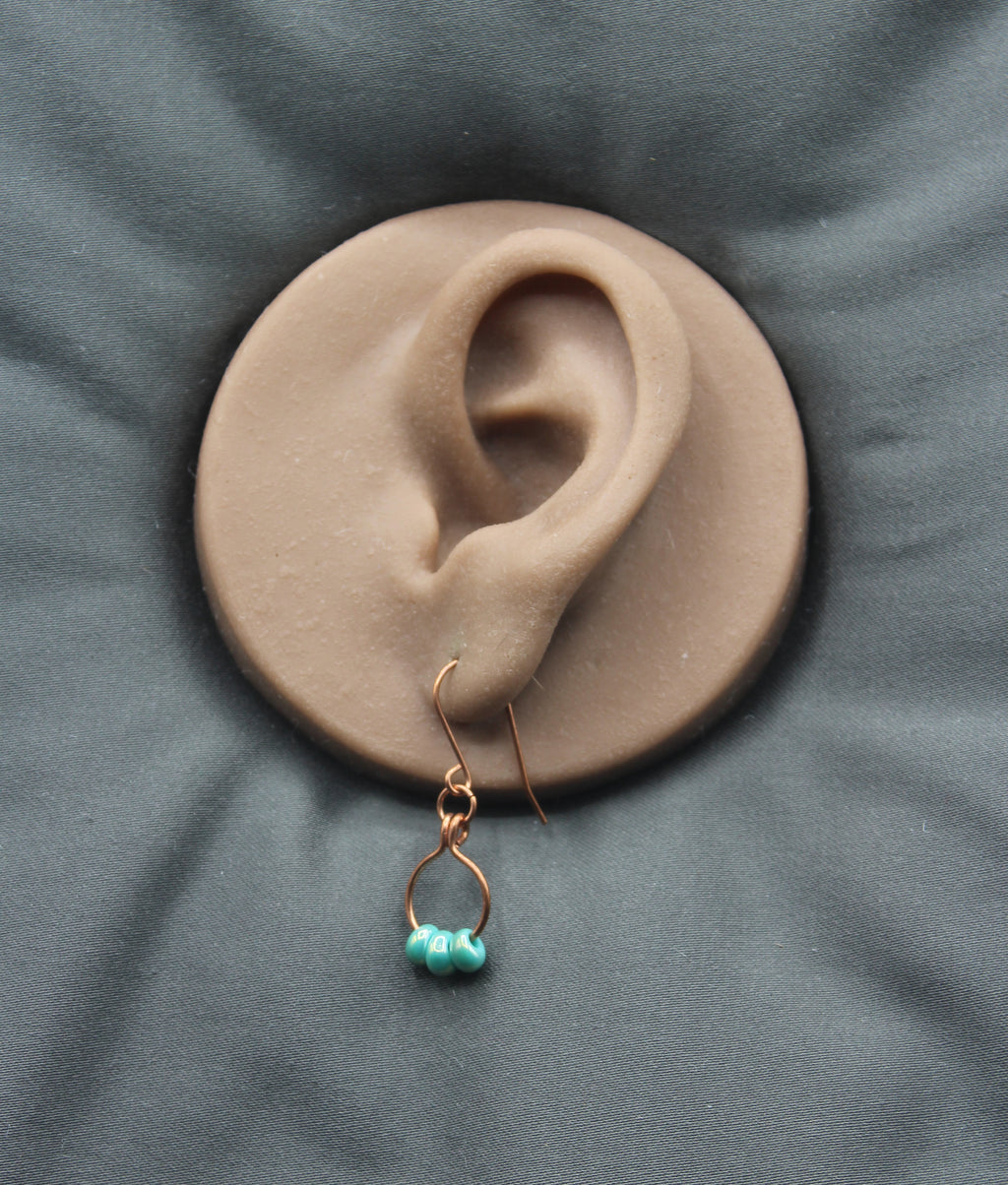 Earring with turquoise beads on a small copper wire hoop, on a clay model of an ear