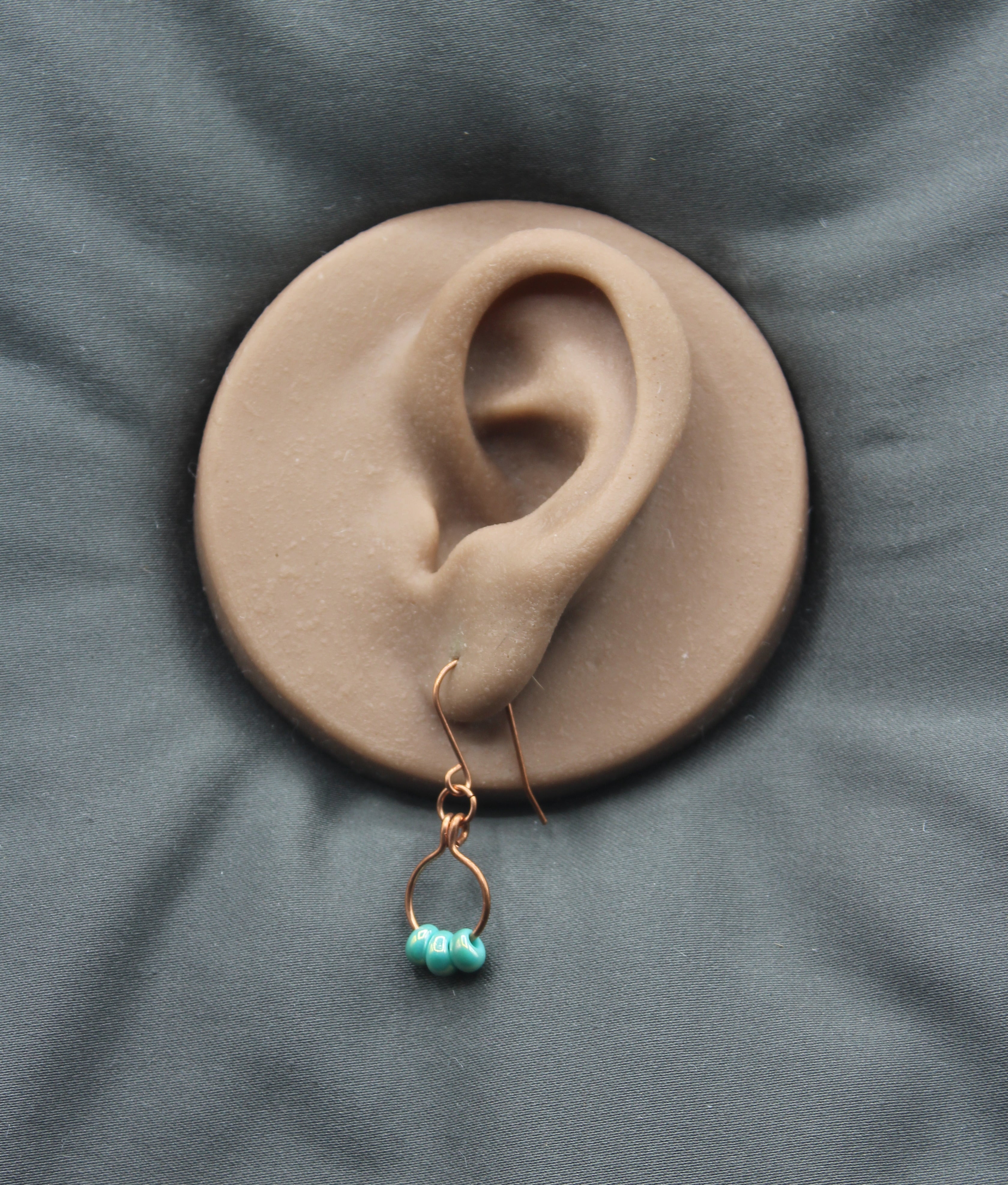 Earring with turquoise beads on a small copper wire hoop, on a clay model of an ear