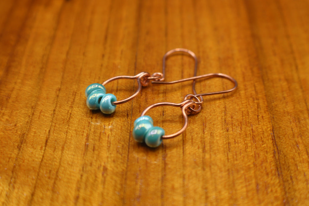 Copper wire earrings with turquoise beads on a wooden surface