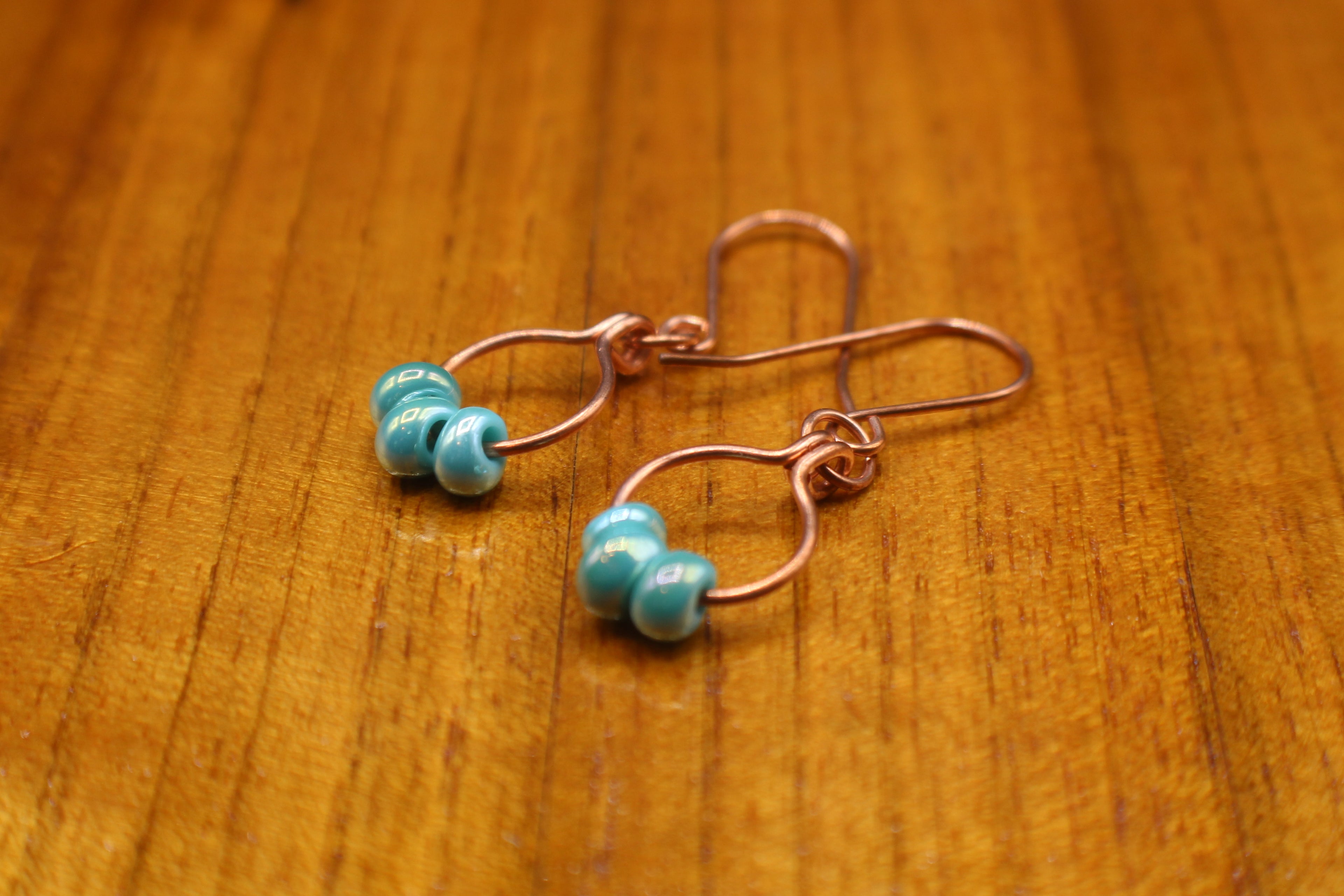 Copper wire earrings with turquoise beads on a wooden surface