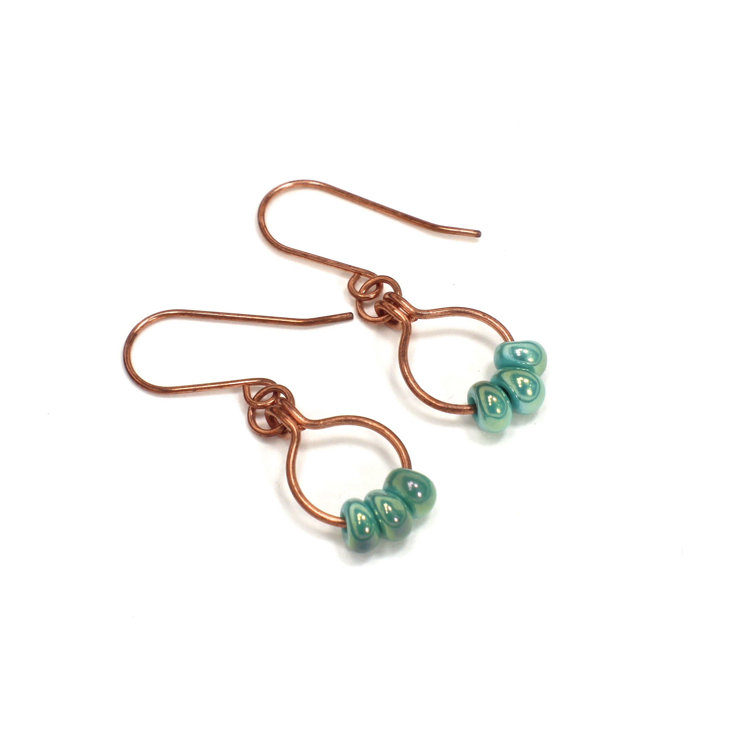 Copper wire earrings with green beads on small hoops, lying on a white background.