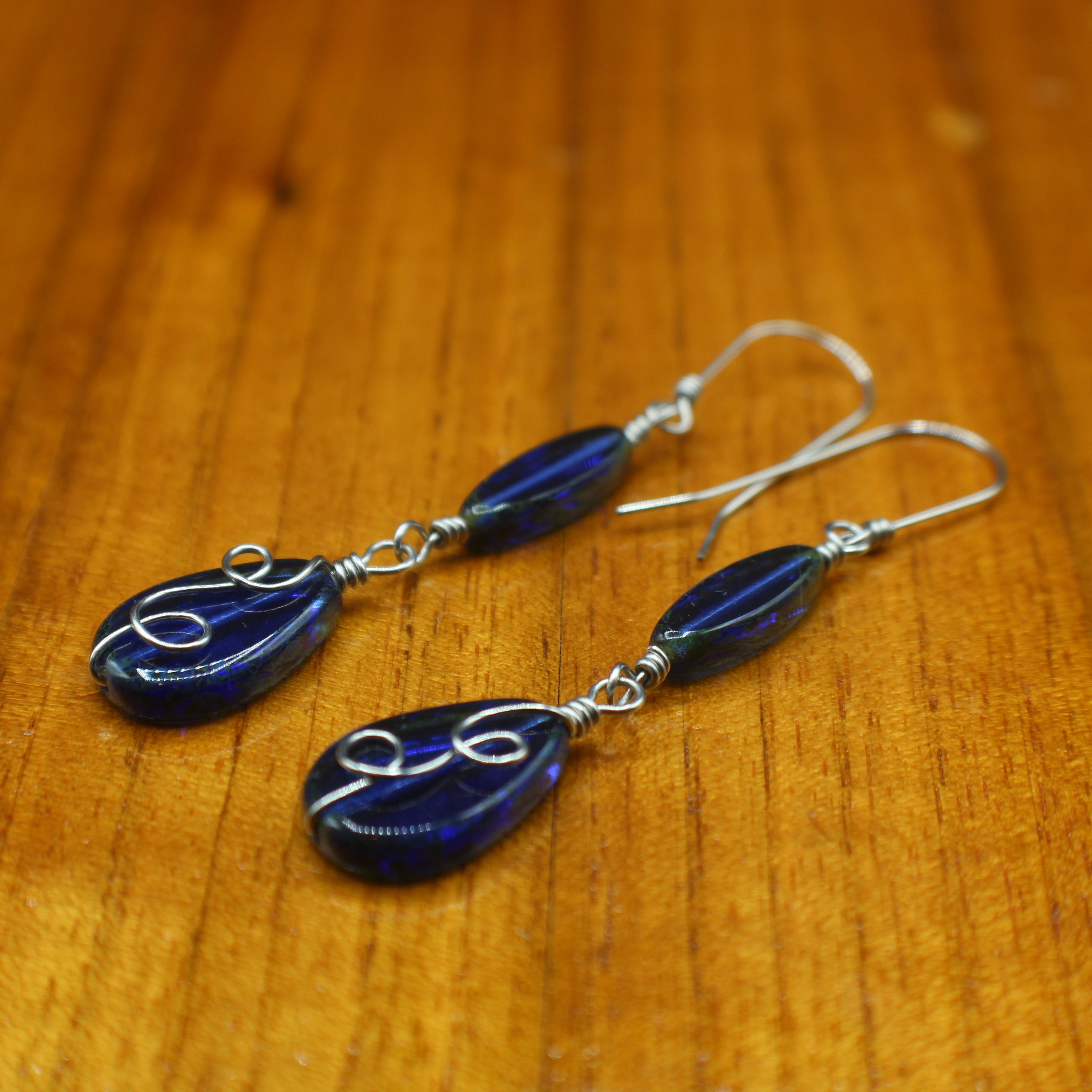 Sapphire blue pair of teardrop earrings with stainless steel details on a wooden surface
