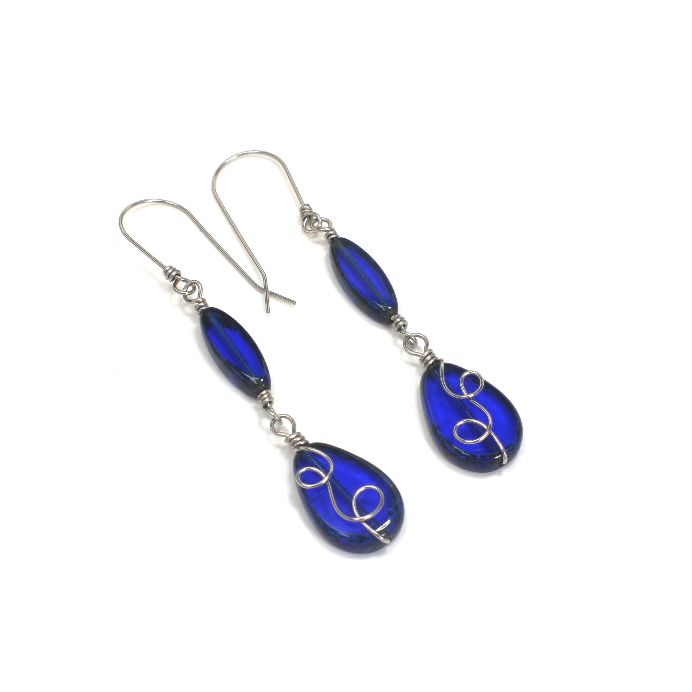 Pair of sapphire blue teardrop earrings with stainless steel wire details on a white background