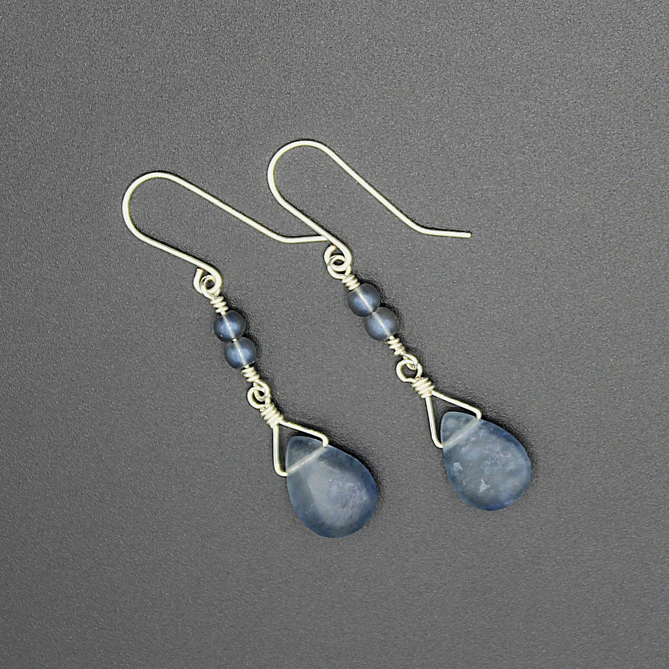 Pair of blue teardrop earrings with wire detailing on a gray background