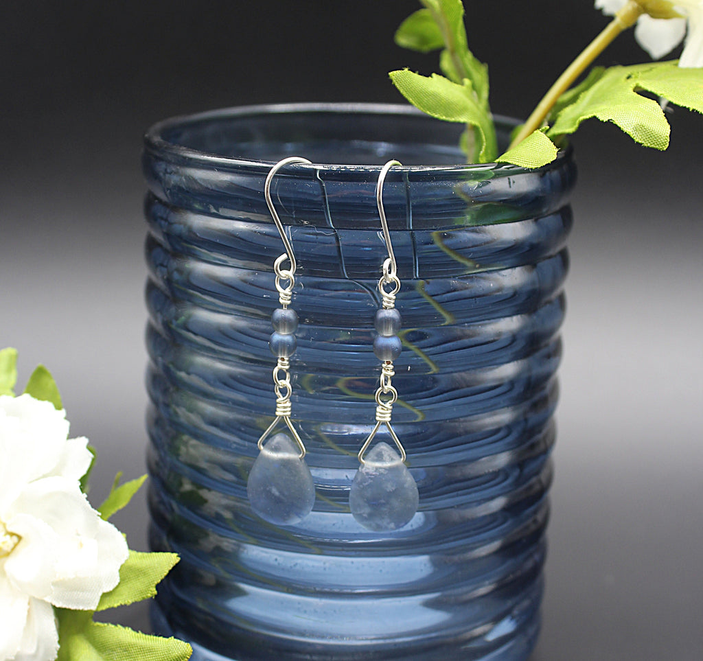 Teardrop-shaped earrings hanging from a blue glass vase with flowers.